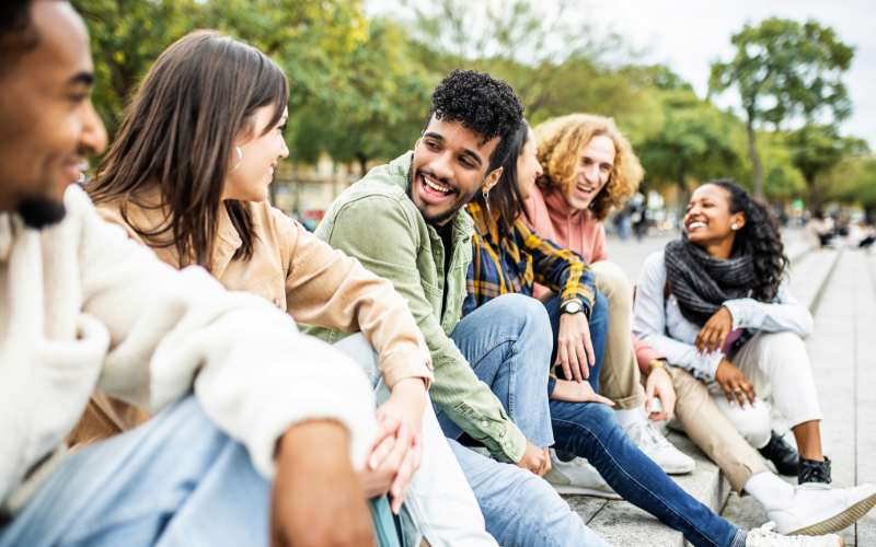 group of young adults sitting on sidewalk talking